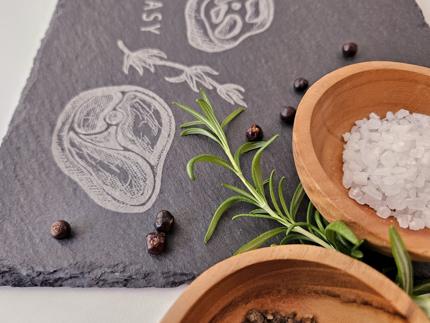 Schieferplatte mit der Aufschrift Steak it easy sowie zwei Steaks und Tymianzweig eingraviert. Zudem Dekoration.