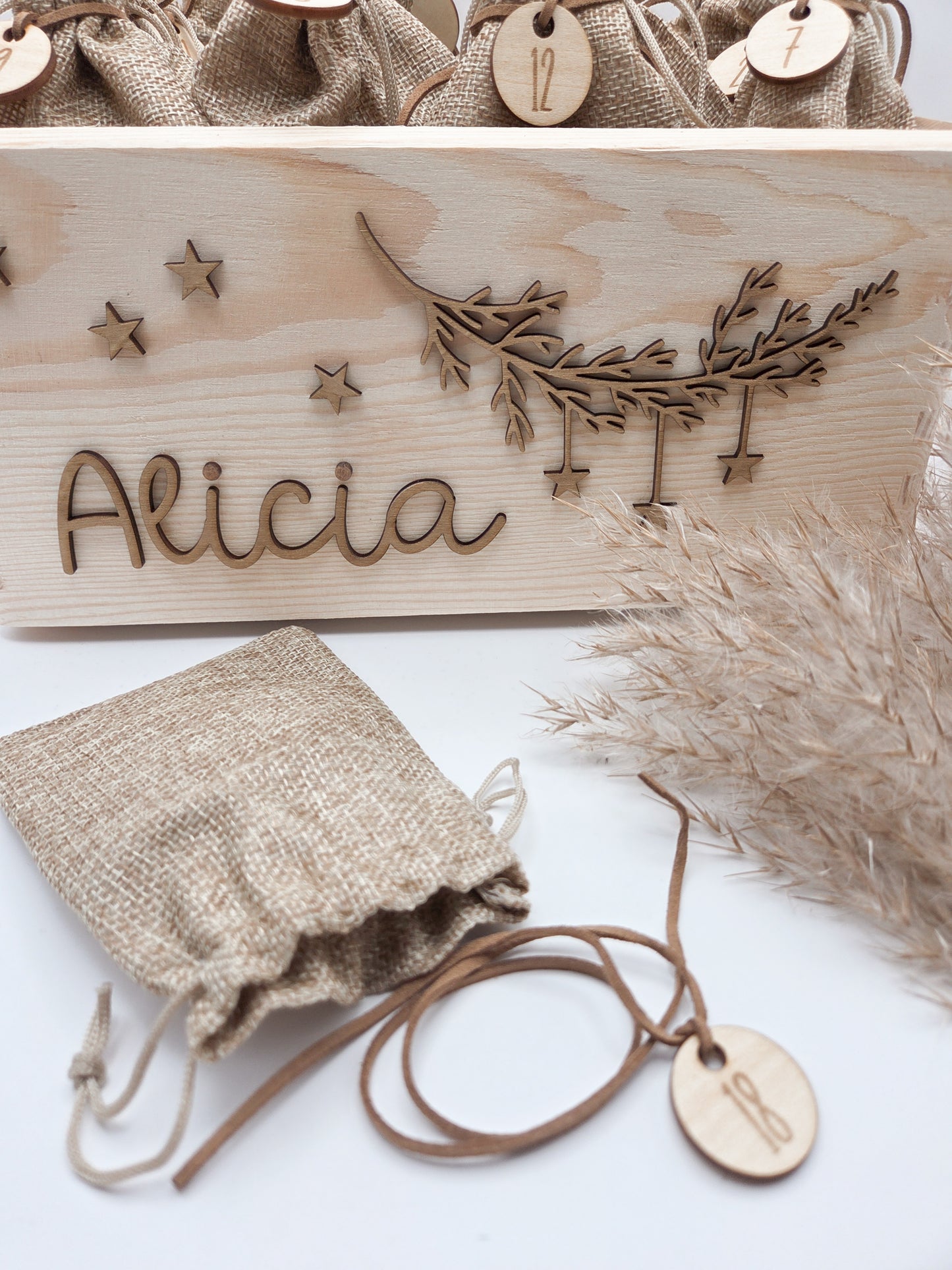 Personalisierte Adventskiste aus hellem Holz mit 3D-Zweig und Sternen, dekoriert mit dem Namen “Alicia”, dazu 24 naturfarbene Jutesäckchen mit gravierten Zahlenanhängern im modernen Scandi-Look.