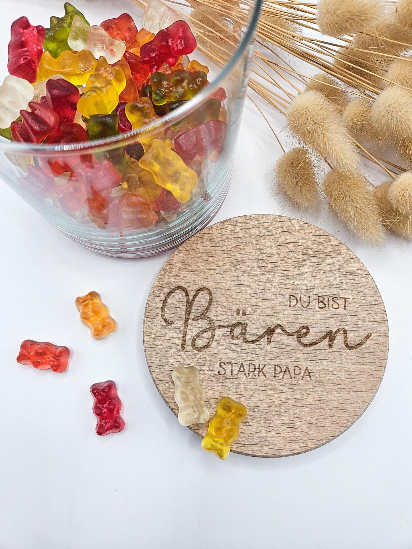 Geschenkglas mit graviertem Holzdeckel für Papa, gefüllt mit hellen Gummibärchen im skandinavischen Stil dekoriert. Der Deckel trägt die liebevolle Gravur „Du bist Bären stark Papa“ mit Herzmotiv. Perfekte Geschenkidee zum Vatertag, Geburtstag oder als kleines Dankeschön für den besten Papa. Modernes, minimalistisches Setting mit Naturmaterialien wie Holz, Trockenblumen und Kerze sorgt für eine warme, hochwertige Präsentation und macht dieses personalisierte Papa Geschenk besonders emotional und einzigartig