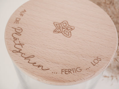 Glas mit Holzdeckel und Gravur „Auf die Plätzchen … fertig … los“ gefüllt mit Weihnachtsplätzchen. Daneben liegen Zimtsterne und Vanillekipferl auf hellem Hintergrund – stimmungsvolles, nordisch-cleanes Weihnachtsmotiv.