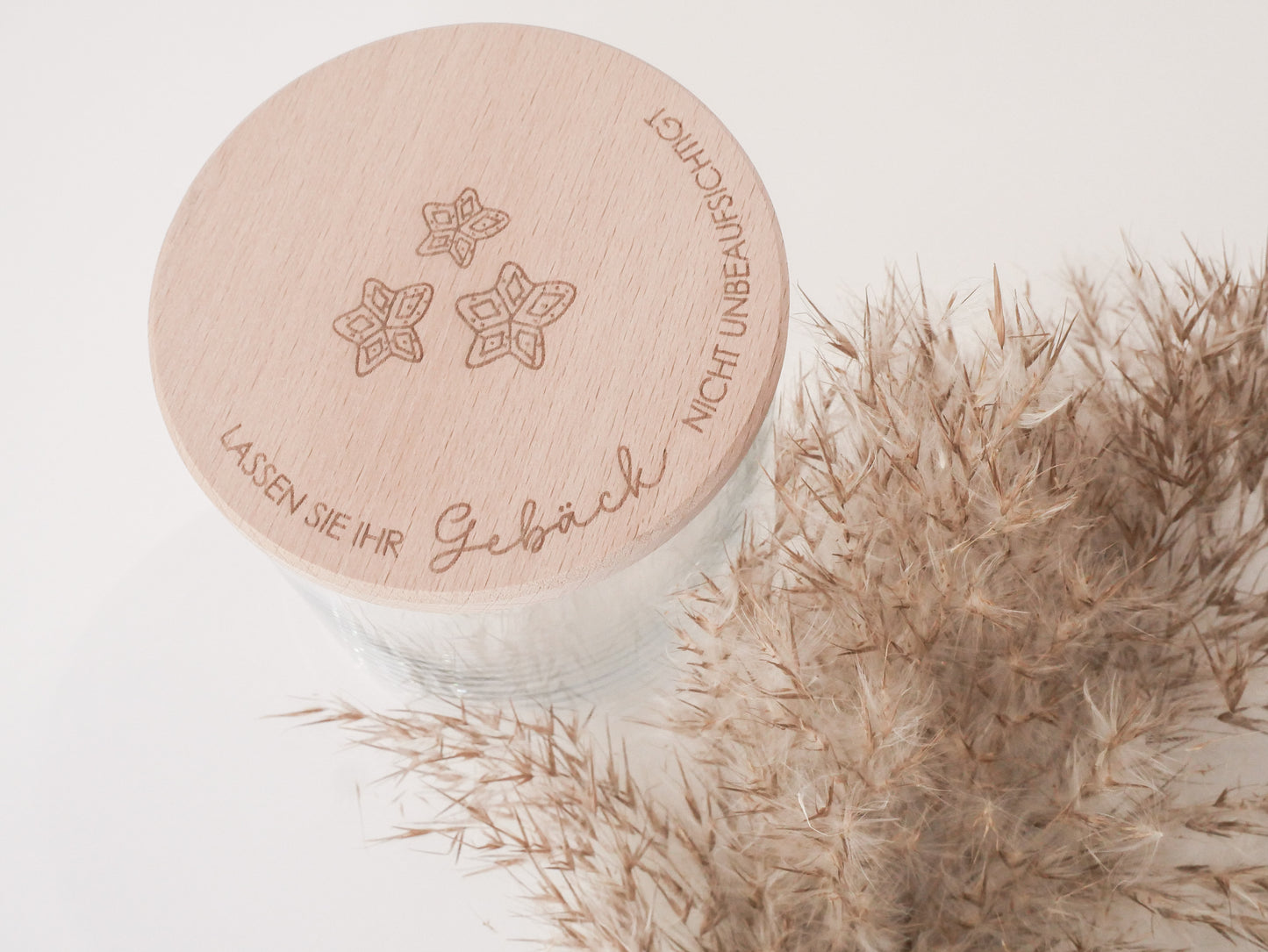 Handgefertigtes Vorratsglas mit graviertem Holzdeckel und Aufschrift „Lassen Sie Ihr Gebäck nicht unbeaufsichtigt“, dekoriert mit feinen Schneeflocken. Ein liebevolles Detail für jede Küche – natürlich, stilvoll und von Leo & Lu.