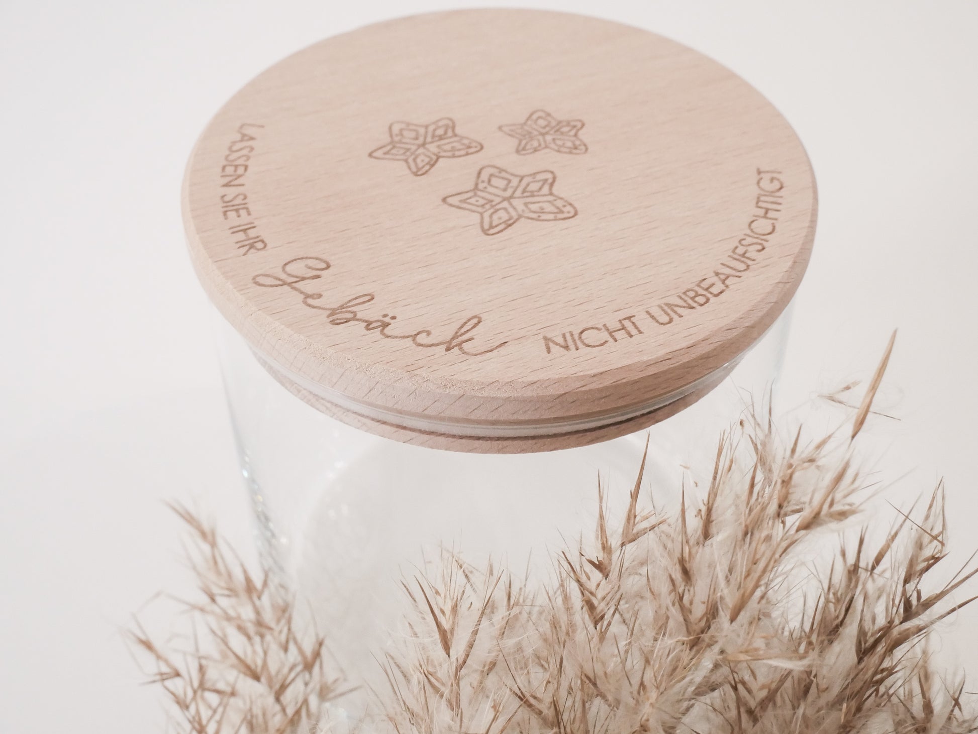 Handgefertigtes Vorratsglas mit graviertem Holzdeckel und Aufschrift „Lassen Sie Ihr Gebäck nicht unbeaufsichtigt“, dekoriert mit feinen Schneeflocken. Ein liebevolles Detail für jede Küche – natürlich, stilvoll und von Leo & Lu.