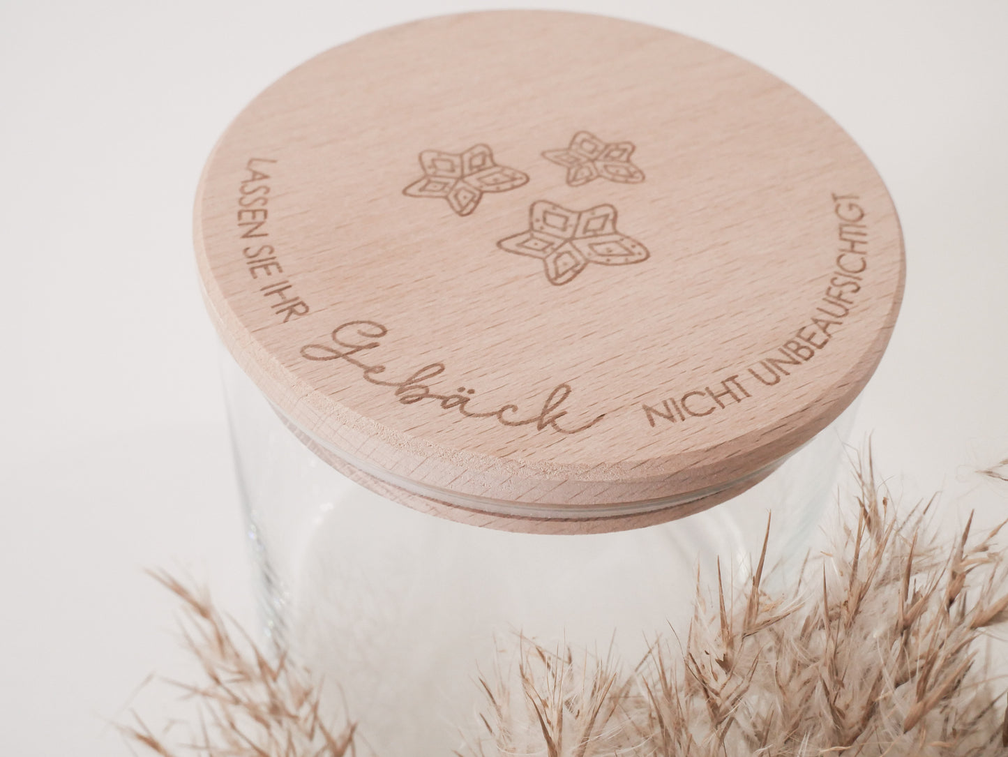 Handgefertigtes Vorratsglas mit graviertem Holzdeckel und Aufschrift „Lassen Sie Ihr Gebäck nicht unbeaufsichtigt“, dekoriert mit feinen Schneeflocken. Ein liebevolles Detail für jede Küche – natürlich, stilvoll und von Leo & Lu.