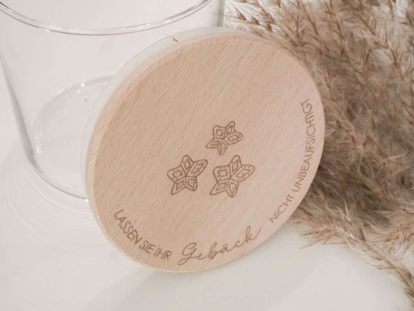 Handgefertigtes Vorratsglas mit graviertem Holzdeckel und Aufschrift „Lassen Sie Ihr Gebäck nicht unbeaufsichtigt“, dekoriert mit feinen Schneeflocken. Ein liebevolles Detail für jede Küche – natürlich, stilvoll und von Leo & Lu.
