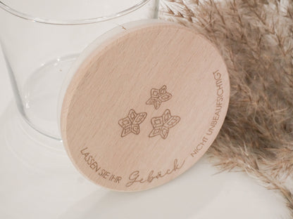Handgefertigtes Vorratsglas mit graviertem Holzdeckel und Aufschrift „Lassen Sie Ihr Gebäck nicht unbeaufsichtigt“, dekoriert mit feinen Schneeflocken. Ein liebevolles Detail für jede Küche – natürlich, stilvoll und von Leo & Lu.
