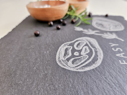 Schieferplatte mit der Aufschrift Steak it easy sowie zwei Steaks und Tymianzweig eingraviert. Zudem Dekoration.