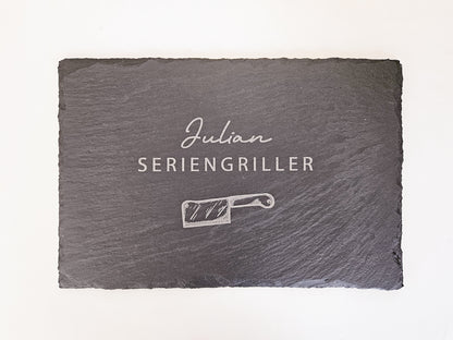Schieferplatte mit personalisiertem Namen hier in dem Beispiel Julian und darunter die Bezeichnung Seriengriller und ein Messer