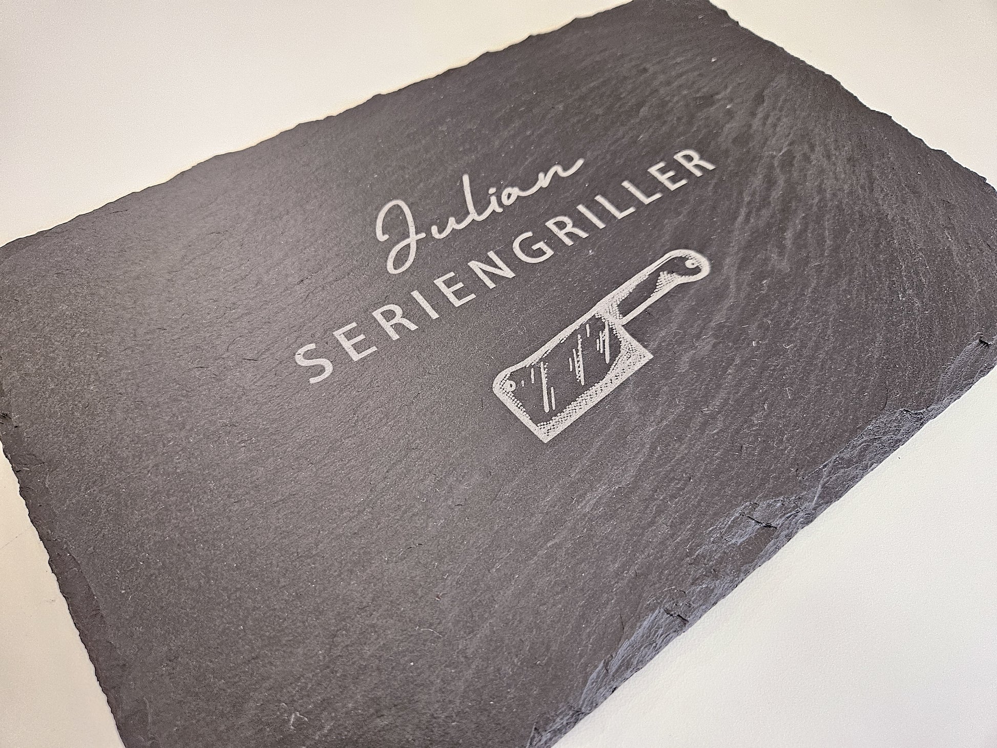 Schieferplatte mit personalisiertem Namen hier in dem Beispiel Julian und darunter die Bezeichnung Seriengriller und ein Messer