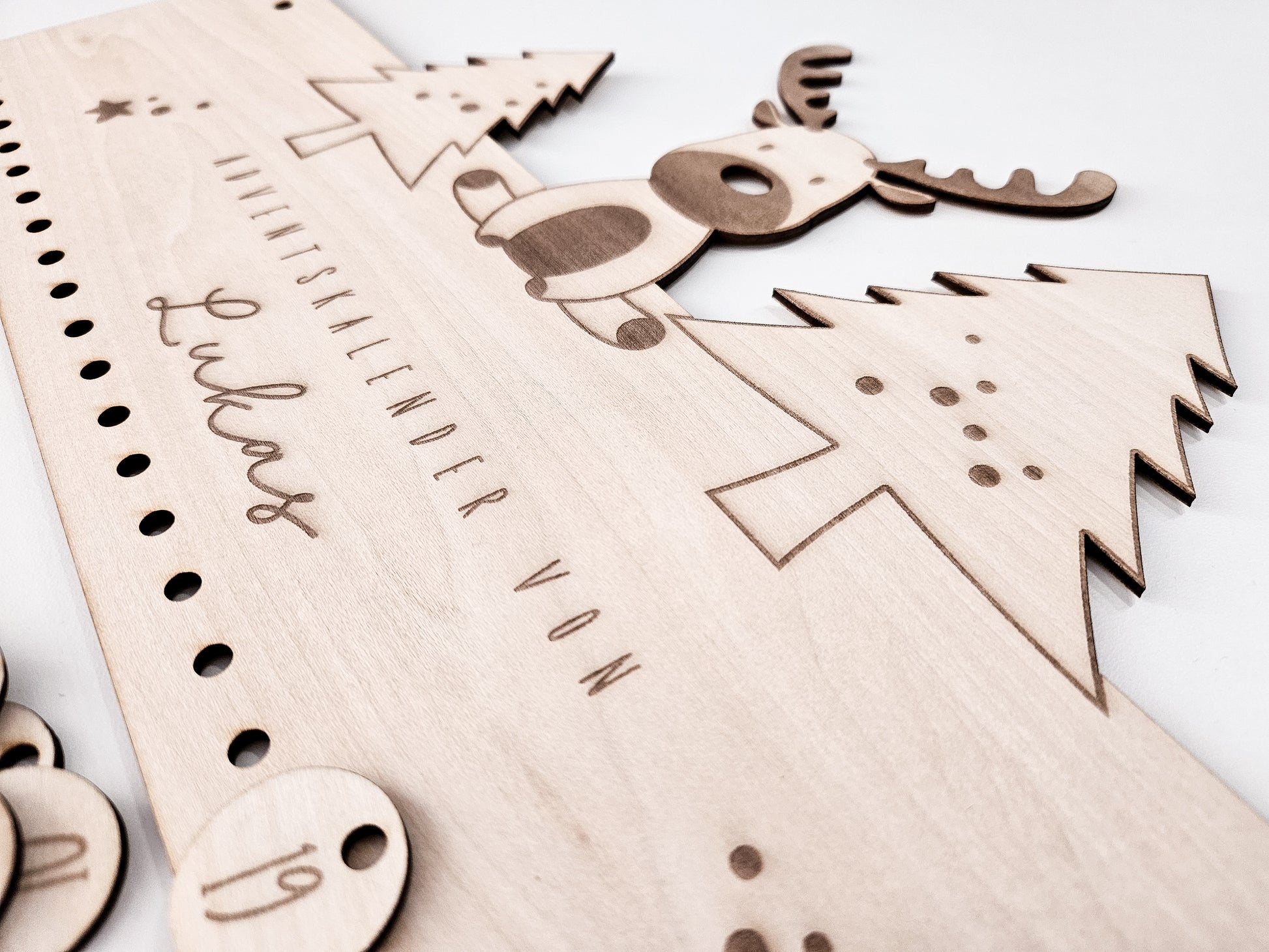 Personalisierter Holz-Adventskalender mit Rentier und Tannenbäumen, Gravur „Adventskalender von Lukas“. Mit 24 nummerierten Holzanhängern zum Aufhängen kleiner Geschenke. Nachhaltige Weihnachtsdekoration für Kinder und Familien.