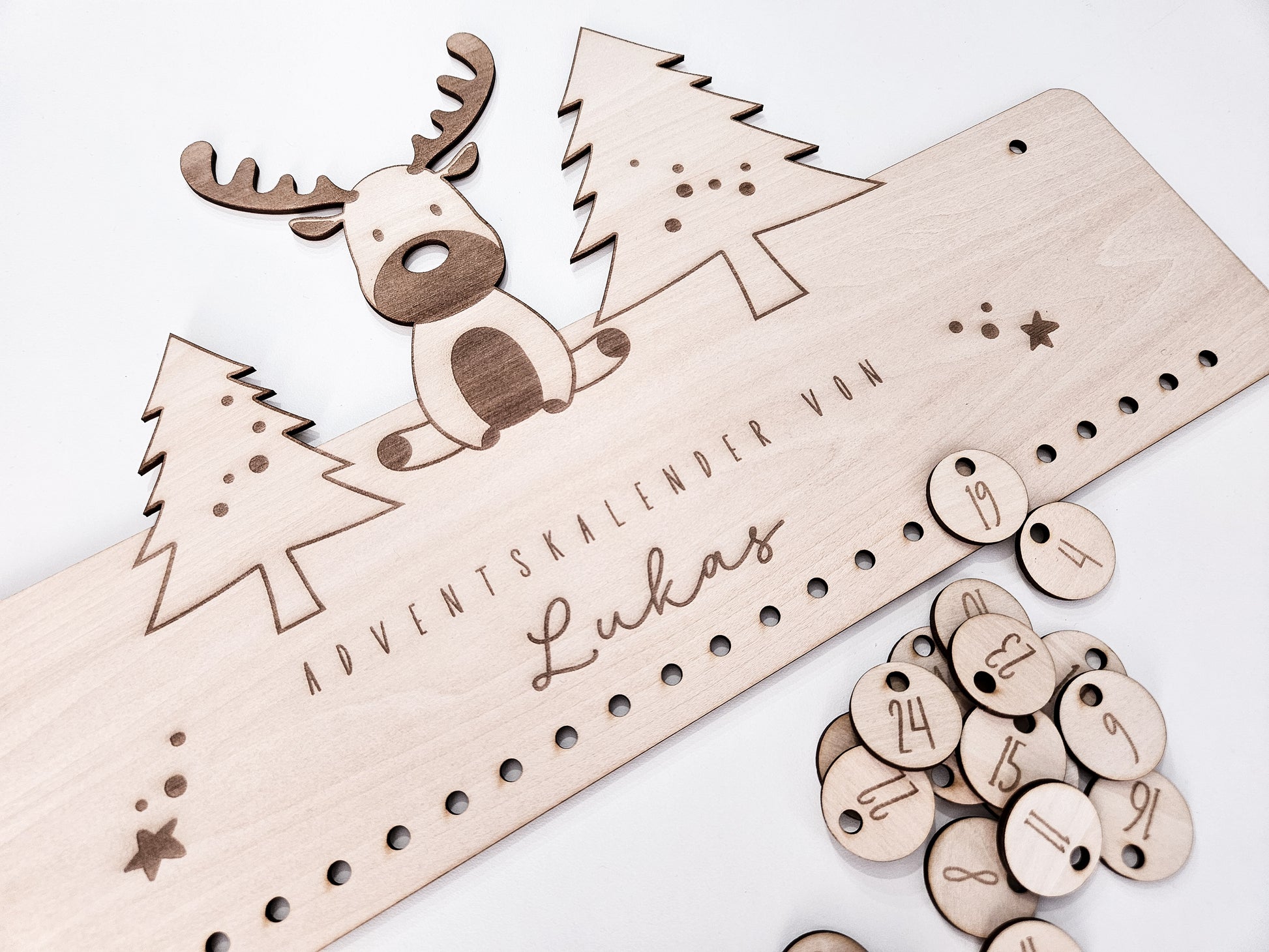 Personalisierter Holz-Adventskalender mit Rentier und Tannenbäumen, Gravur „Adventskalender von Lukas“. Mit 24 nummerierten Holzanhängern zum Aufhängen kleiner Geschenke. Nachhaltige Weihnachtsdekoration für Kinder und Familien.