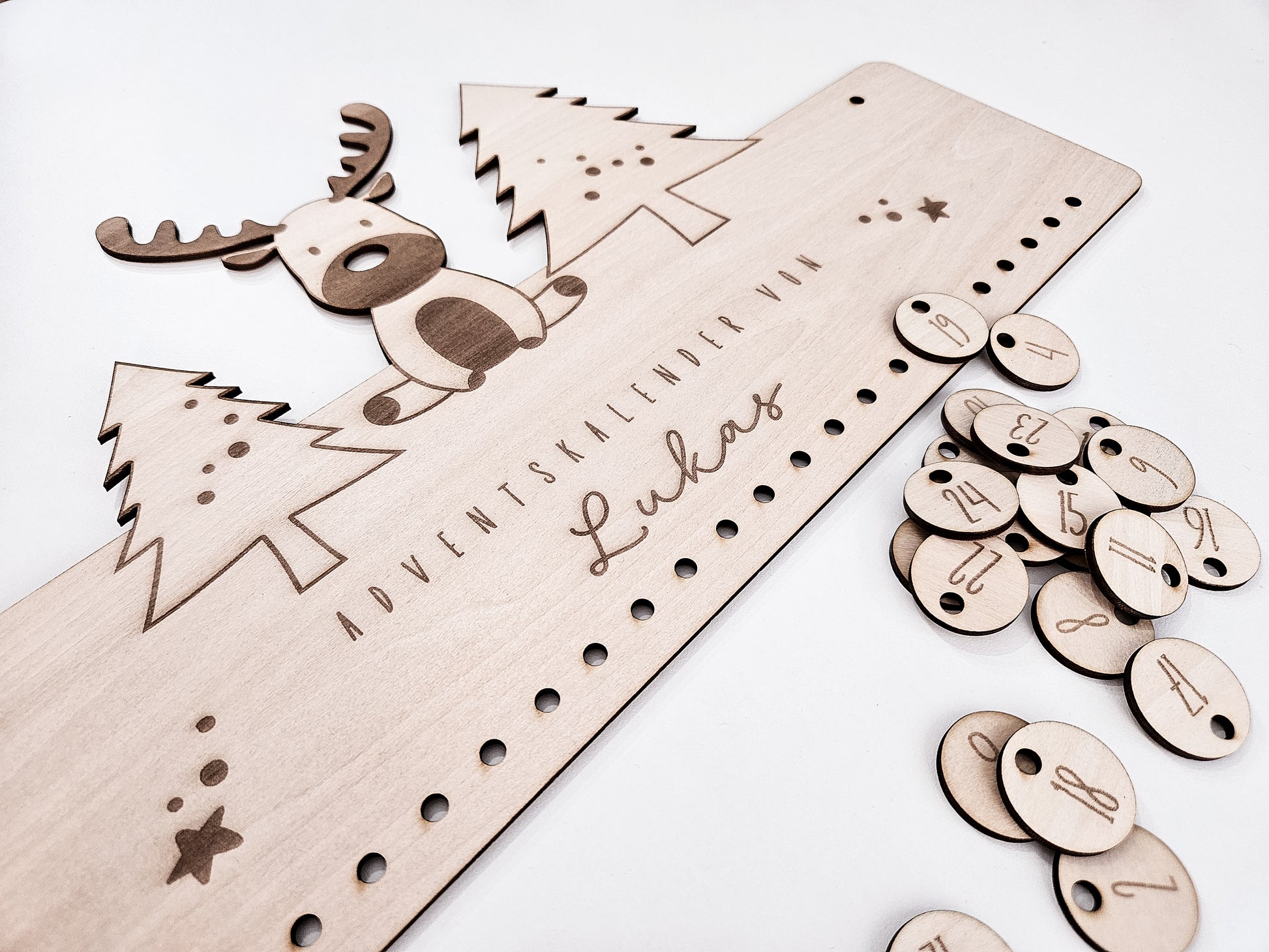Personalisierter Holz-Adventskalender mit Rentier und Tannenbäumen, Gravur „Adventskalender von Lukas“. Mit 24 nummerierten Holzanhängern zum Aufhängen kleiner Geschenke. Nachhaltige Weihnachtsdekoration für Kinder und Familien.