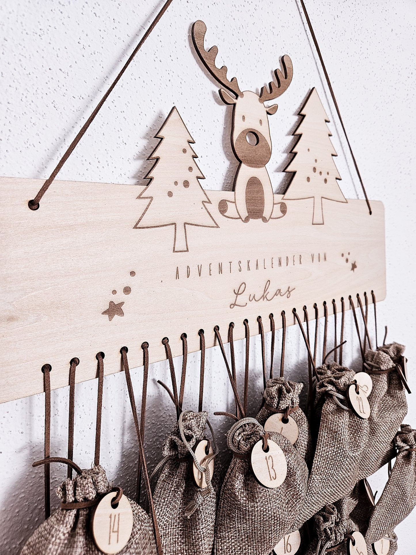 Personalisierter Holz-Adventskalender mit Rentier und Tannenbäumen, Gravur „Adventskalender von Lukas“. Mit 24 nummerierten Holzanhängern zum Aufhängen kleiner Geschenke. Nachhaltige Weihnachtsdekoration für Kinder und Familien.
