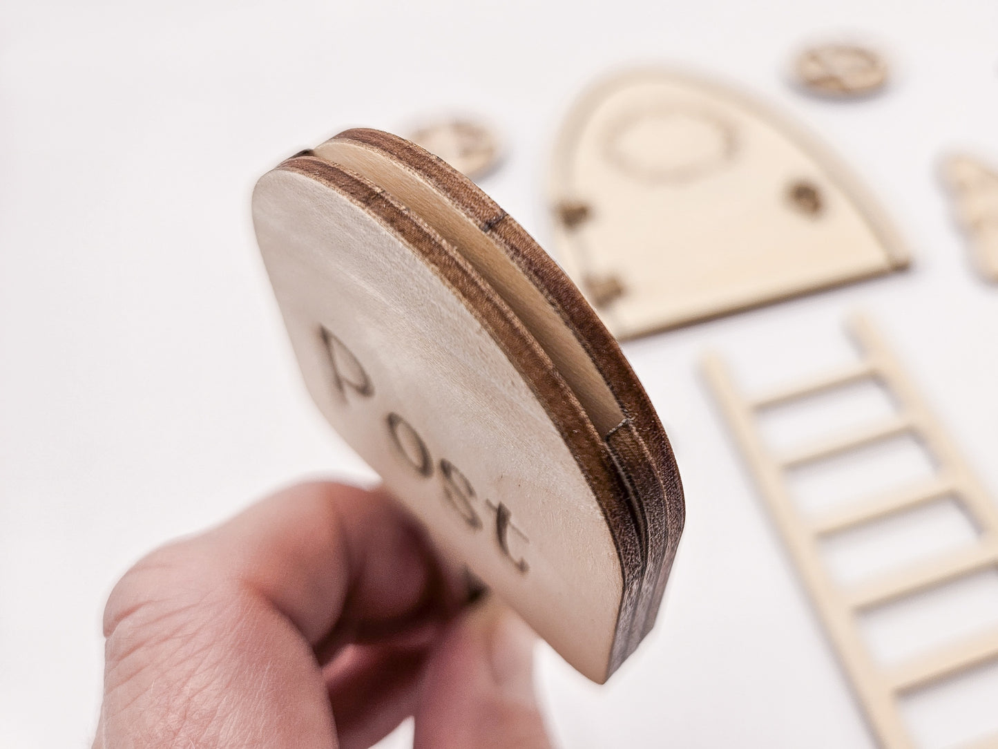 Personalisierbare Holz-Wichteltür mit Leiter, Briefkasten, Pilz und zwei Tannenbäumen an einer weißen Sockelleiste im Kinderzimmer, auf hellblauer Wand mit weißen Punkten montiert.