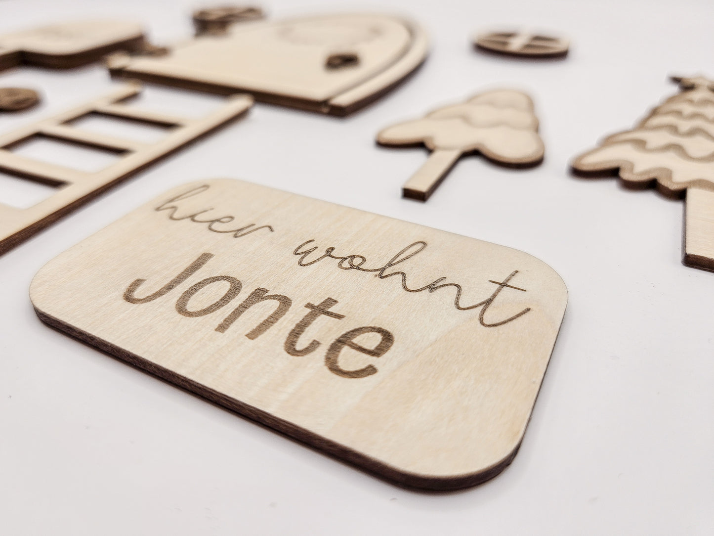 Personalisierbare Holz-Wichteltür mit Leiter, Briefkasten, Pilz und zwei Tannenbäumen an einer weißen Sockelleiste im Kinderzimmer, auf hellblauer Wand mit weißen Punkten montiert.