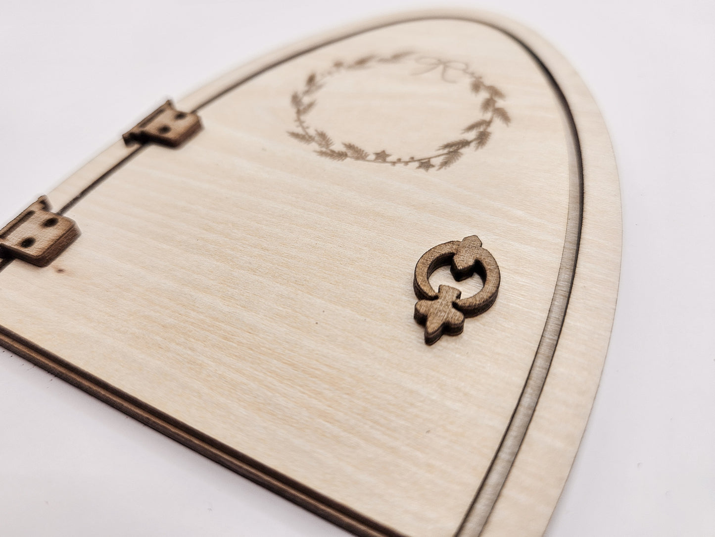 Personalisierbare Holz-Wichteltür mit Leiter, Briefkasten, Pilz und zwei Tannenbäumen an einer weißen Sockelleiste im Kinderzimmer, auf hellblauer Wand mit weißen Punkten montiert.