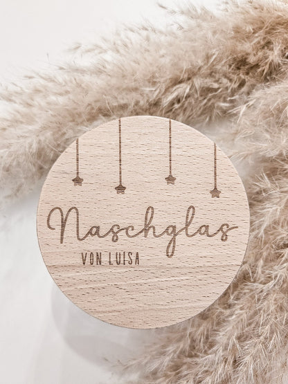 Runder Holzdeckel mit graviertem Schriftzug „Naschglas von Luisa“ und Sternanhängern, auf Glas liegend – personalisierte Geschenkidee.