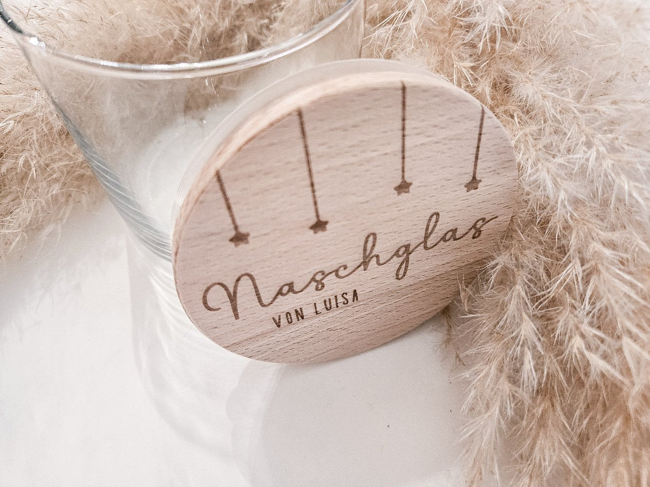 Runder Holzdeckel mit graviertem Schriftzug „Naschglas von Luisa“ und Sternanhängern, auf Glas liegend – personalisierte Geschenkidee.
