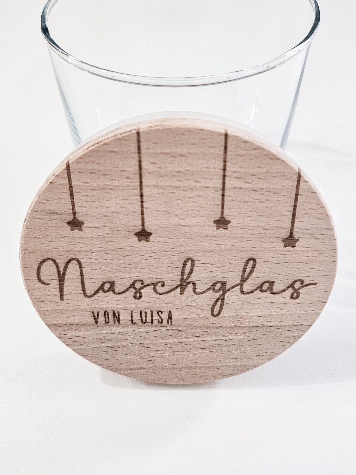 Runder Holzdeckel mit graviertem Schriftzug „Naschglas von Luisa“ und Sternanhängern, auf Glas liegend – personalisierte Geschenkidee.