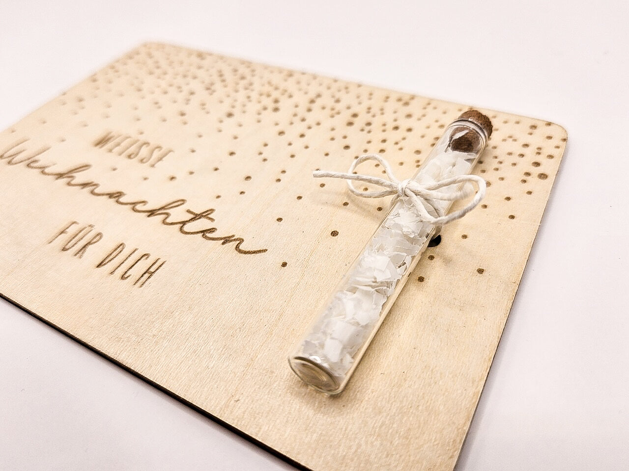 Holzkarte „Weiße Weihnachten“ mit Glasröhrchen, Gravur und winterlicher Deko im skandinavischen Stil auf hellem Holztisch