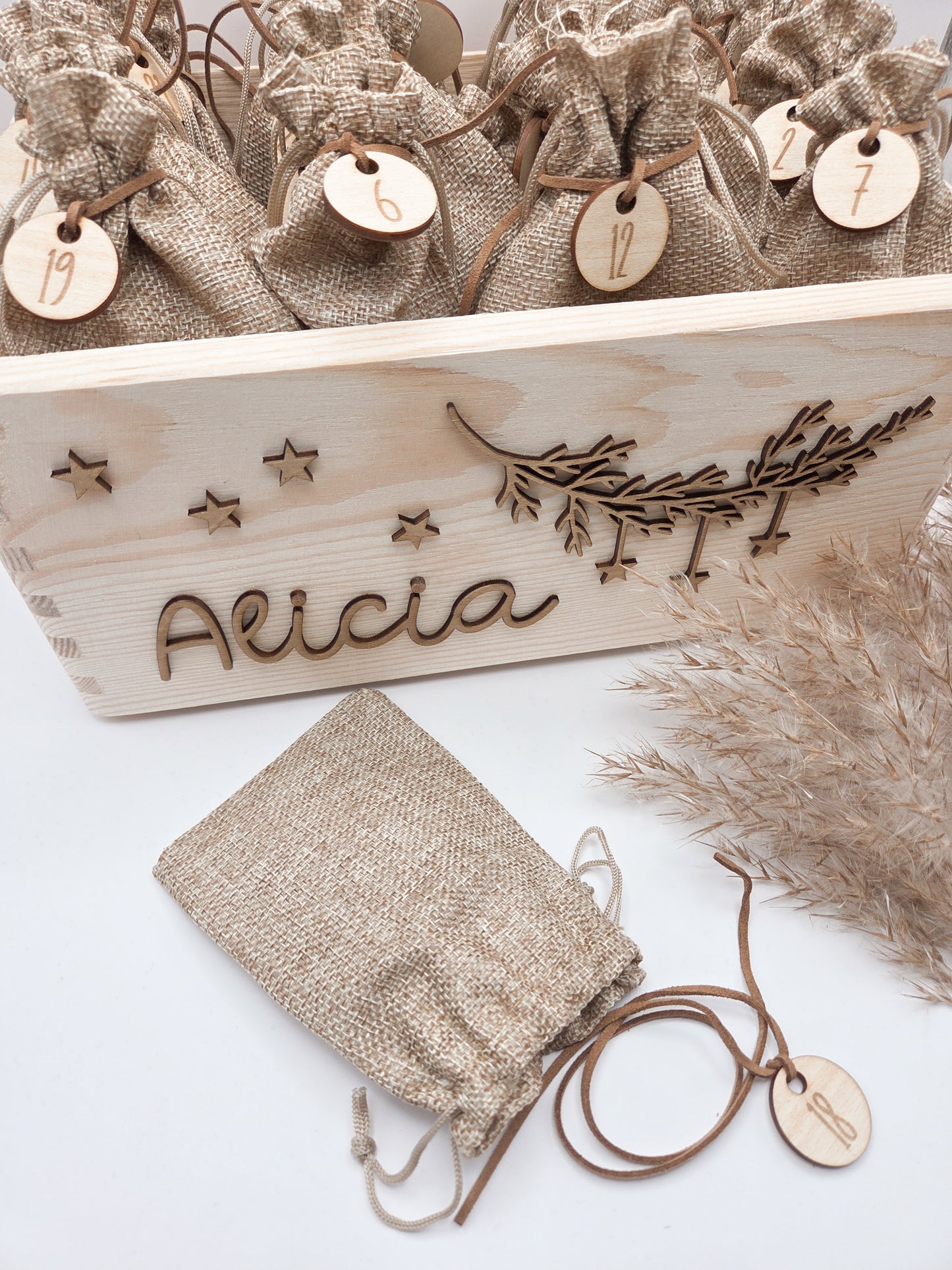 Personalisierte Adventskiste aus hellem Holz mit 3D-Zweig und Sternen, dekoriert mit dem Namen “Alicia”, dazu 24 naturfarbene Jutesäckchen mit gravierten Zahlenanhängern im modernen Scandi-Look.