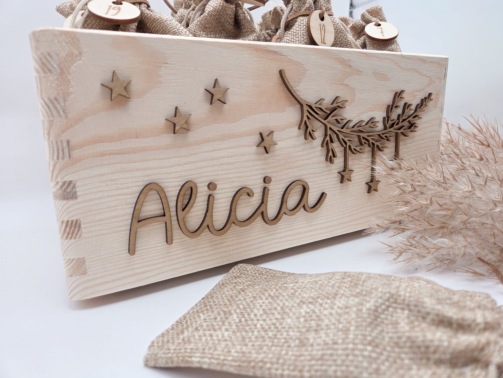 Personalisierte Adventskiste aus hellem Holz mit 3D-Zweig und Sternen, dekoriert mit dem Namen “Alicia”, dazu 24 naturfarbene Jutesäckchen mit gravierten Zahlenanhängern im modernen Scandi-Look.