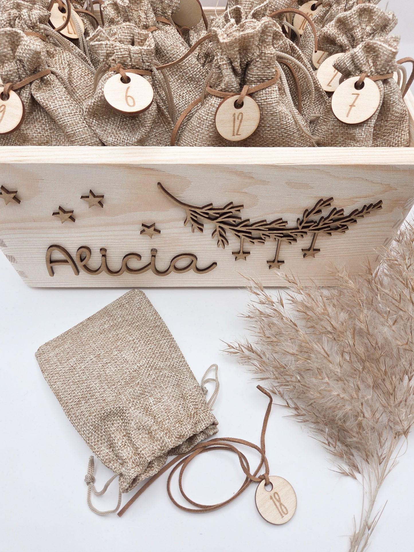 Personalisierte Adventskiste aus hellem Holz mit 3D-Zweig und Sternen, dekoriert mit dem Namen “Alicia”, dazu 24 naturfarbene Jutesäckchen mit gravierten Zahlenanhängern im modernen Scandi-Look.