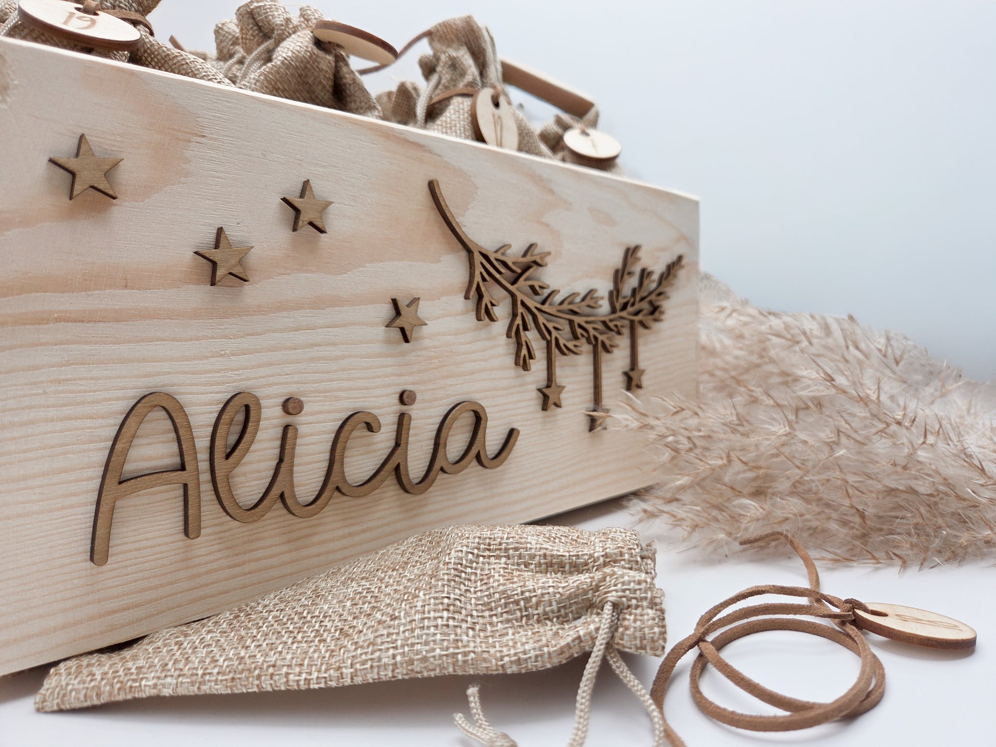 Personalisierte Adventskiste aus hellem Holz mit 3D-Zweig und Sternen, dekoriert mit dem Namen “Alicia”, dazu 24 naturfarbene Jutesäckchen mit gravierten Zahlenanhängern im modernen Scandi-Look.