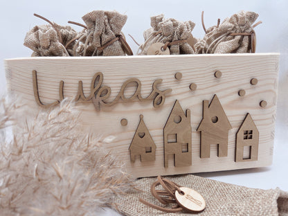Personalisierte Adventskiste aus Holz mit 3D-Weihnachtsdorf, 24 Jutesäckchen und Zahlenanhängern im hellen skandinavischen Leo&Lu-Stil.