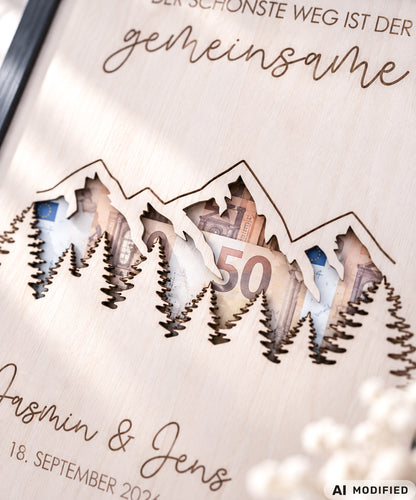 Personalisiertes Geldgeschenk zur Hochzeit aus Holz mit filigran ausgeschnittener Berg- und Waldlandschaft. Hinter den Bergen lassen sich Geldscheine dekorativ platzieren. Mit Gravur „Der schönste Weg ist der gemeinsame“, Namen des Brautpaares und Hochzeitsdatum. Originelles Hochzeitsgeschenk für Braut und Bräutigam, ideal als Geldgeschenk zur Hochzeit, personalisierte Hochzeitsdeko und besondere Geschenkidee für Paare, Bergliebhaber, Wanderfreunde und Naturliebhaber.