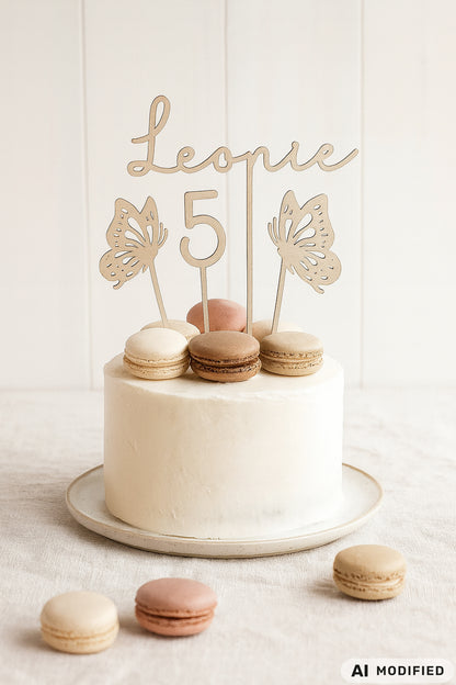 Personalisierter Cake Topper aus Holz mit dem Namen „Leonie“, einer großen Zahl 5 und zwei filigranen Schmetterlingen als Tortenstecker für den 5. Geburtstag. Der hochwertige Holzstecker schmückt eine schlichte weiße Torte, dekoriert mit Macarons in Creme-, Beige- und Rosétönen. Das moderne, minimalistische Design in natürlicher Holzoptik eignet sich ideal für Kindergeburtstage, Einschulungen oder besondere Familienfeiern und setzt stilvolle Akzente auf jeder Geburtstagstorte.