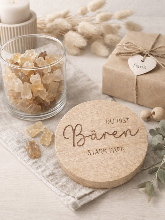 Geschenkglas mit graviertem Holzdeckel für Papa, gefüllt mit hellen Gummibärchen im skandinavischen Stil dekoriert. Der Deckel trägt die liebevolle Gravur „Du bist Bären stark Papa“ mit Herzmotiv. Perfekte Geschenkidee zum Vatertag, Geburtstag oder als kleines Dankeschön für den besten Papa. Modernes, minimalistisches Setting mit Naturmaterialien wie Holz, Trockenblumen und Kerze sorgt für eine warme, hochwertige Präsentation und macht dieses personalisierte Papa Geschenk besonders emotional und einzigartig