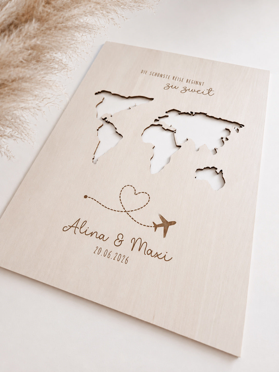 Personalisiertes Geldgeschenk zur Hochzeit aus hellem Holz mit filigraner Weltkarte und eingesteckten Euro-Geldscheinen hinter den Kontinenten. Die gravierte Aufschrift „Die schönste Reise beginnt zu zweit“ sowie die Namen des Brautpaares und das Hochzeitsdatum machen dieses Hochzeitsgeschenk zu einer besonderen Erinnerung. Das Holzbild steht in einer romantischen Hochzeitskulisse mit weißen Rosen, Kerzenlicht, Eheringen und eleganter Tischdekoration. Perfekt als Geldgeschenk für Flitterwochen, Reisekasse o