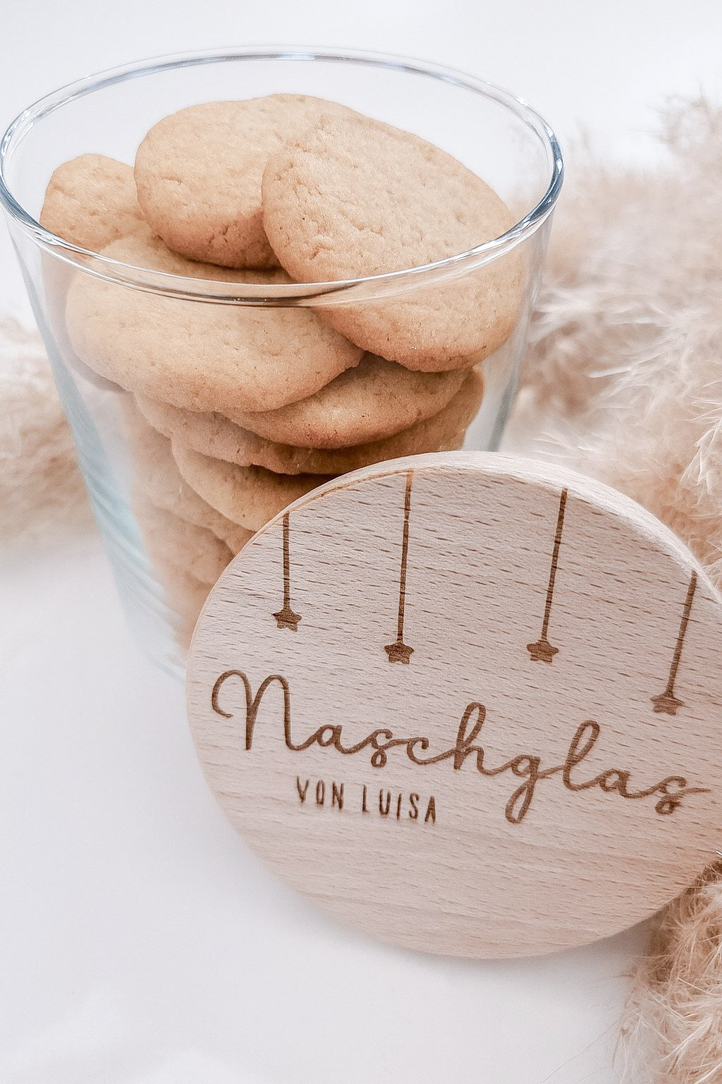 Runder Holzdeckel mit graviertem Schriftzug „Naschglas von Luisa“ und Sternanhängern, auf Glas liegend – personalisierte Geschenkidee.