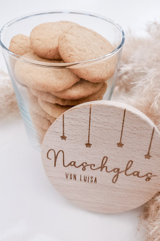 Runder Holzdeckel mit graviertem Schriftzug „Naschglas von Luisa“ und Sternanhängern, auf Glas liegend – personalisierte Geschenkidee.