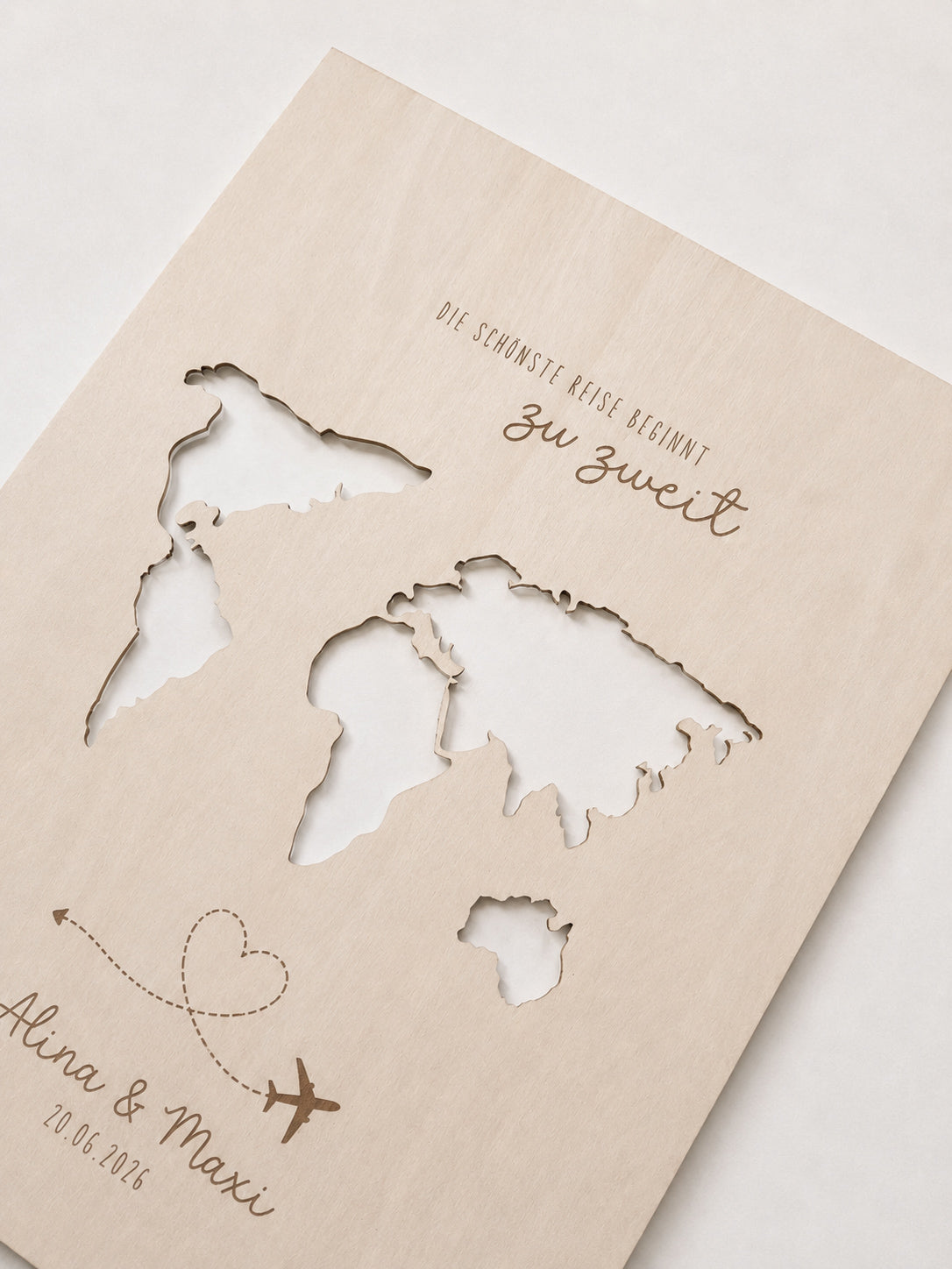 Personalisiertes Geldgeschenk zur Hochzeit aus hellem Holz mit filigraner Weltkarte und eingesteckten Euro-Geldscheinen hinter den Kontinenten. Die gravierte Aufschrift „Die schönste Reise beginnt zu zweit“ sowie die Namen des Brautpaares und das Hochzeitsdatum machen dieses Hochzeitsgeschenk zu einer besonderen Erinnerung. Das Holzbild steht in einer romantischen Hochzeitskulisse mit weißen Rosen, Kerzenlicht, Eheringen und eleganter Tischdekoration. Perfekt als Geldgeschenk für Flitterwochen, Reisekasse o