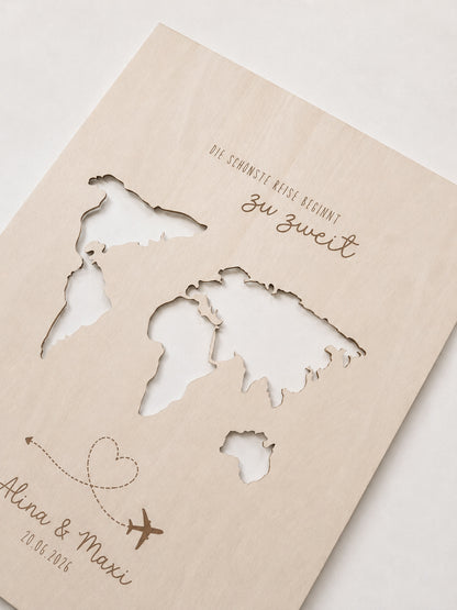 Personalisiertes Geldgeschenk zur Hochzeit aus hellem Holz mit filigraner Weltkarte und eingesteckten Euro-Geldscheinen hinter den Kontinenten. Die gravierte Aufschrift „Die schönste Reise beginnt zu zweit“ sowie die Namen des Brautpaares und das Hochzeitsdatum machen dieses Hochzeitsgeschenk zu einer besonderen Erinnerung. Das Holzbild steht in einer romantischen Hochzeitskulisse mit weißen Rosen, Kerzenlicht, Eheringen und eleganter Tischdekoration. Perfekt als Geldgeschenk für Flitterwochen, Reisekasse o