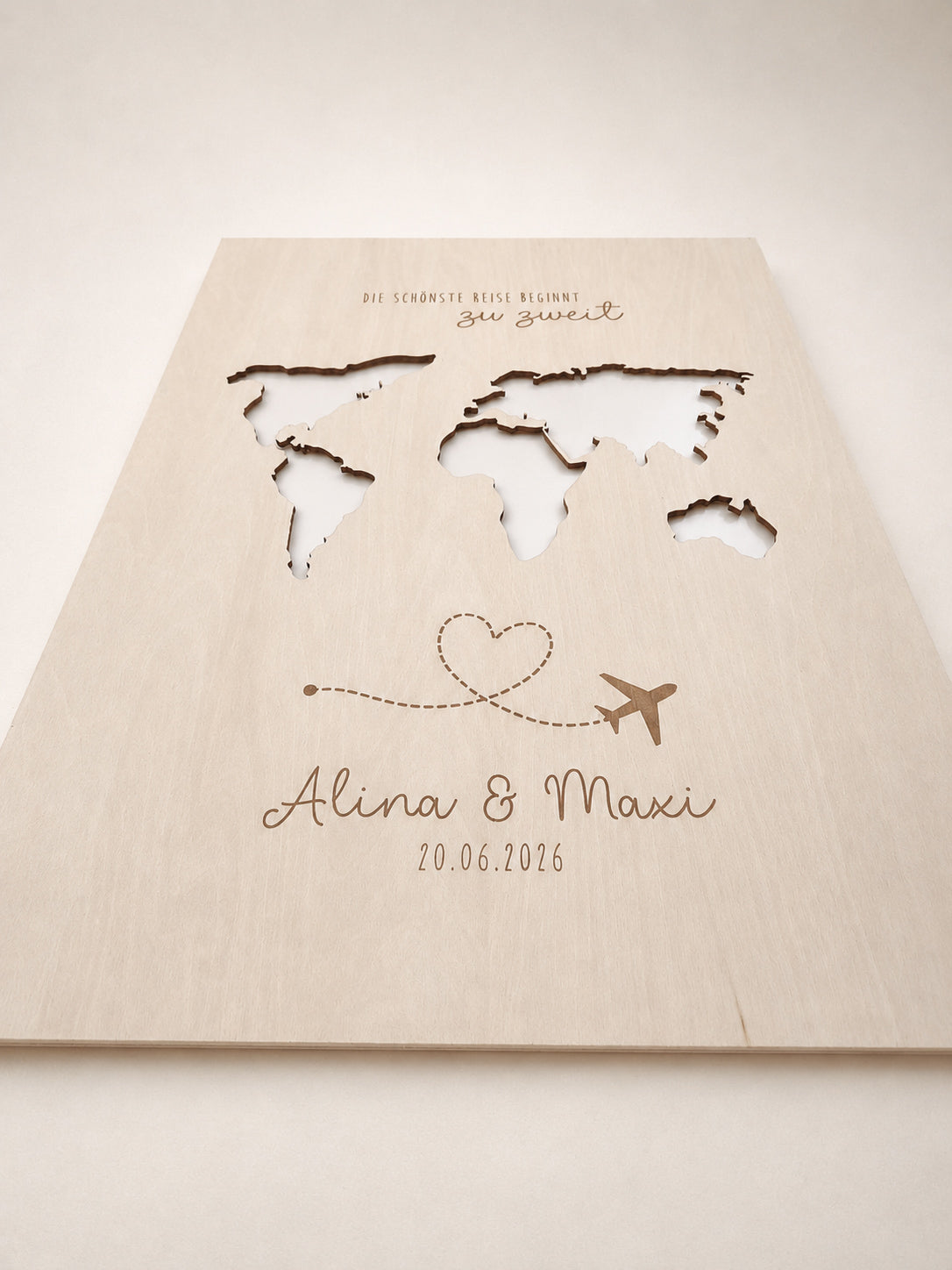 Personalisiertes Geldgeschenk zur Hochzeit aus hellem Holz mit filigraner Weltkarte und eingesteckten Euro-Geldscheinen hinter den Kontinenten. Die gravierte Aufschrift „Die schönste Reise beginnt zu zweit“ sowie die Namen des Brautpaares und das Hochzeitsdatum machen dieses Hochzeitsgeschenk zu einer besonderen Erinnerung. Das Holzbild steht in einer romantischen Hochzeitskulisse mit weißen Rosen, Kerzenlicht, Eheringen und eleganter Tischdekoration. Perfekt als Geldgeschenk für Flitterwochen, Reisekasse o