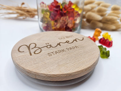 Geschenkglas mit graviertem Holzdeckel für Papa, gefüllt mit hellen Gummibärchen im skandinavischen Stil dekoriert. Der Deckel trägt die liebevolle Gravur „Du bist Bären stark Papa“ mit Herzmotiv. Perfekte Geschenkidee zum Vatertag, Geburtstag oder als kleines Dankeschön für den besten Papa. Modernes, minimalistisches Setting mit Naturmaterialien wie Holz, Trockenblumen und Kerze sorgt für eine warme, hochwertige Präsentation und macht dieses personalisierte Papa Geschenk besonders emotional und einzigartig