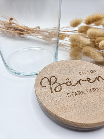Geschenkglas mit graviertem Holzdeckel für Papa, gefüllt mit hellen Gummibärchen im skandinavischen Stil dekoriert. Der Deckel trägt die liebevolle Gravur „Du bist Bären stark Papa“ mit Herzmotiv. Perfekte Geschenkidee zum Vatertag, Geburtstag oder als kleines Dankeschön für den besten Papa. Modernes, minimalistisches Setting mit Naturmaterialien wie Holz, Trockenblumen und Kerze sorgt für eine warme, hochwertige Präsentation und macht dieses personalisierte Papa Geschenk besonders emotional und einzigartig