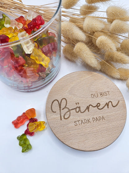 Geschenkglas mit graviertem Holzdeckel für Papa, gefüllt mit hellen Gummibärchen im skandinavischen Stil dekoriert. Der Deckel trägt die liebevolle Gravur „Du bist Bären stark Papa“ mit Herzmotiv. Perfekte Geschenkidee zum Vatertag, Geburtstag oder als kleines Dankeschön für den besten Papa. Modernes, minimalistisches Setting mit Naturmaterialien wie Holz, Trockenblumen und Kerze sorgt für eine warme, hochwertige Präsentation und macht dieses personalisierte Papa Geschenk besonders emotional und einzigartig