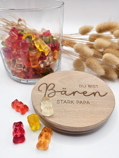Geschenkglas mit graviertem Holzdeckel für Papa, gefüllt mit hellen Gummibärchen im skandinavischen Stil dekoriert. Der Deckel trägt die liebevolle Gravur „Du bist Bären stark Papa“ mit Herzmotiv. Perfekte Geschenkidee zum Vatertag, Geburtstag oder als kleines Dankeschön für den besten Papa. Modernes, minimalistisches Setting mit Naturmaterialien wie Holz, Trockenblumen und Kerze sorgt für eine warme, hochwertige Präsentation und macht dieses personalisierte Papa Geschenk besonders emotional und einzigartig