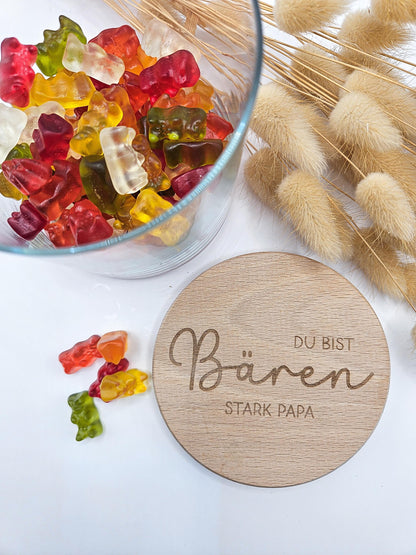 Geschenkglas mit graviertem Holzdeckel für Papa, gefüllt mit hellen Gummibärchen im skandinavischen Stil dekoriert. Der Deckel trägt die liebevolle Gravur „Du bist Bären stark Papa“ mit Herzmotiv. Perfekte Geschenkidee zum Vatertag, Geburtstag oder als kleines Dankeschön für den besten Papa. Modernes, minimalistisches Setting mit Naturmaterialien wie Holz, Trockenblumen und Kerze sorgt für eine warme, hochwertige Präsentation und macht dieses personalisierte Papa Geschenk besonders emotional und einzigartig