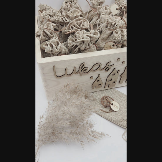 Personalisierte Adventskiste aus Holz mit 3D-Weihnachtsdorf, 24 Jutesäckchen und Zahlenanhängern im hellen skandinavischen Leo&Lu-Stil.