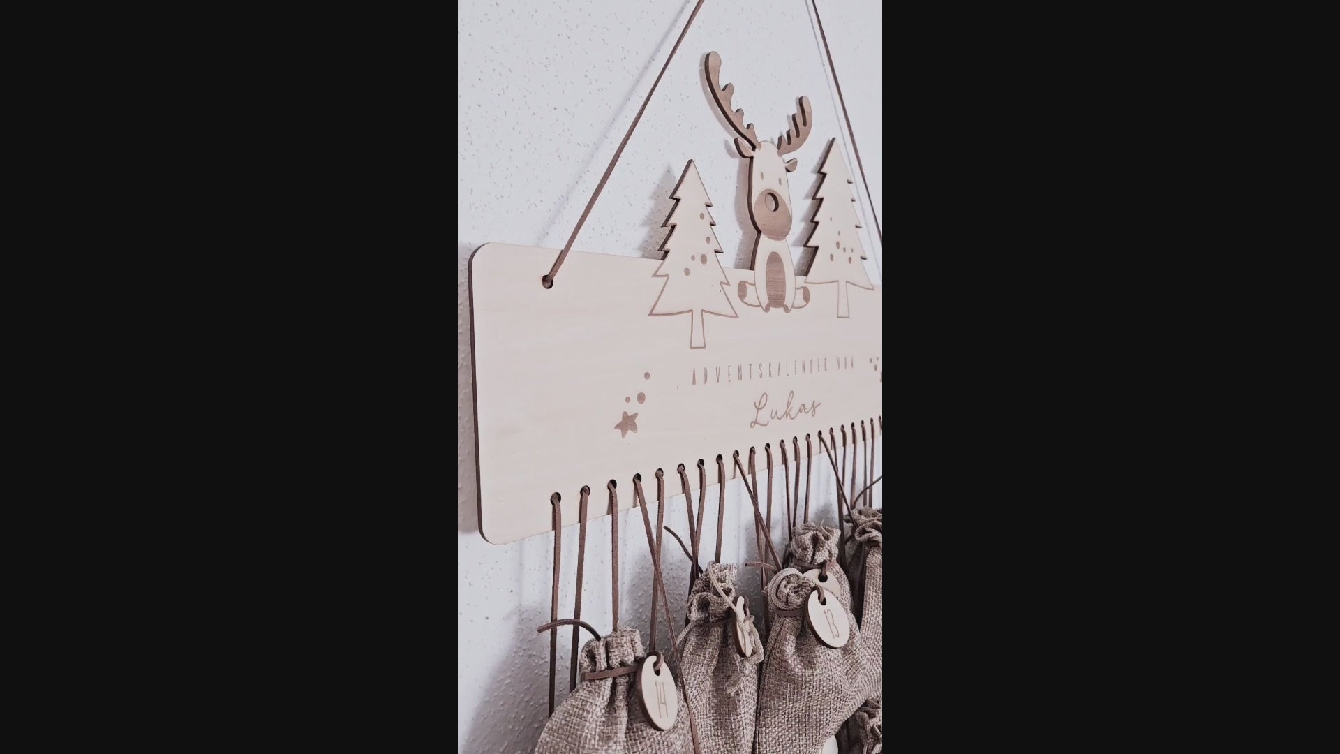 Personalisierter Holz-Adventskalender mit Rentier und Tannenbäumen, Gravur „Adventskalender von Lukas“. Mit 24 nummerierten Holzanhängern zum Aufhängen kleiner Geschenke. Nachhaltige Weihnachtsdekoration für Kinder und Familien.