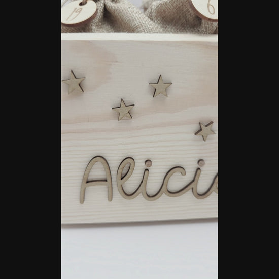 Personalisierte Adventskiste aus hellem Holz mit 3D-Zweig und Sternen, dekoriert mit dem Namen “Alicia”, dazu 24 naturfarbene Jutesäckchen mit gravierten Zahlenanhängern im modernen Scandi-Look.