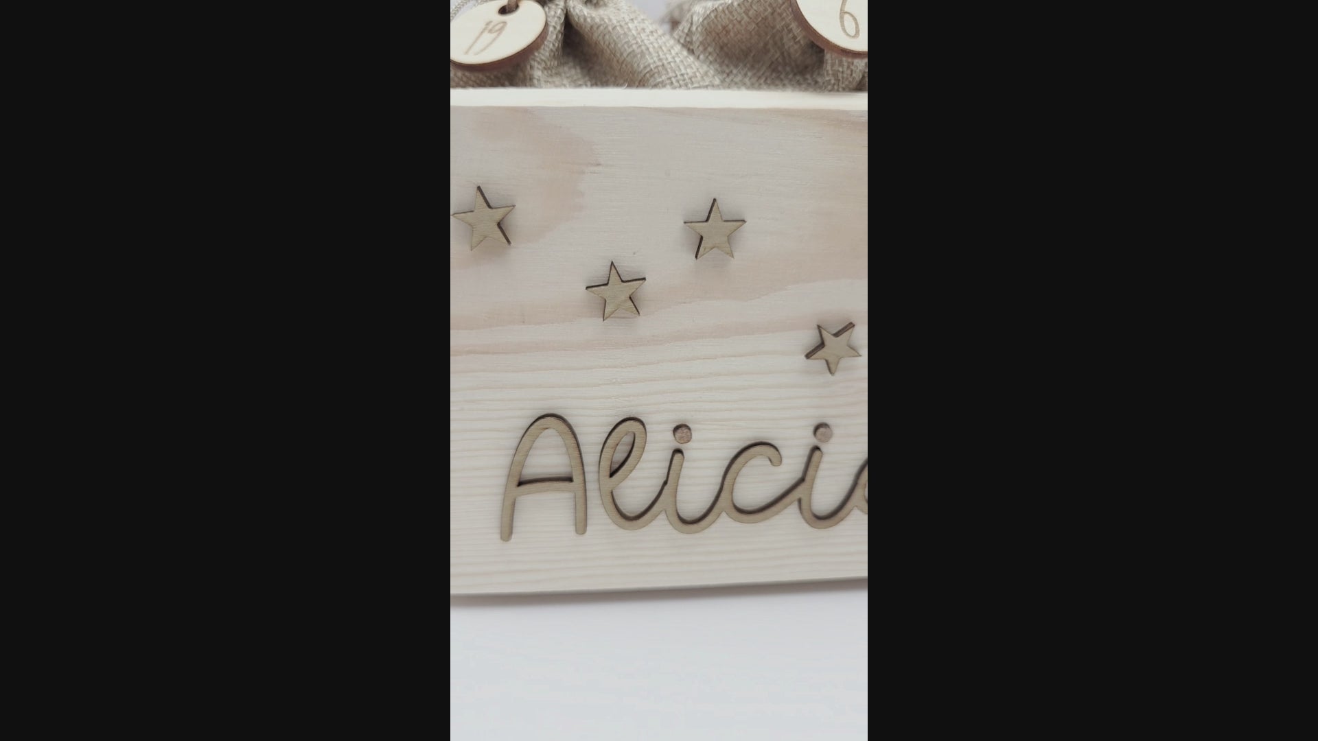 Personalisierte Adventskiste aus hellem Holz mit 3D-Zweig und Sternen, dekoriert mit dem Namen “Alicia”, dazu 24 naturfarbene Jutesäckchen mit gravierten Zahlenanhängern im modernen Scandi-Look.
